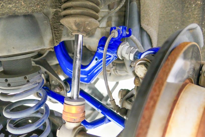 Close-up of a car suspension system with blue control arm and metal components.